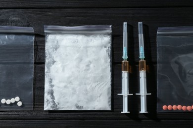 Photo of Drug addiction. Plastic bag with powder, syringes and pills on black wooden table, flat lay