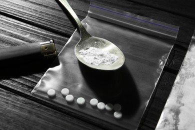 Photo of Drug addiction. Spoon bag with powder, cigarette lighter and pills on black wooden table, closeup