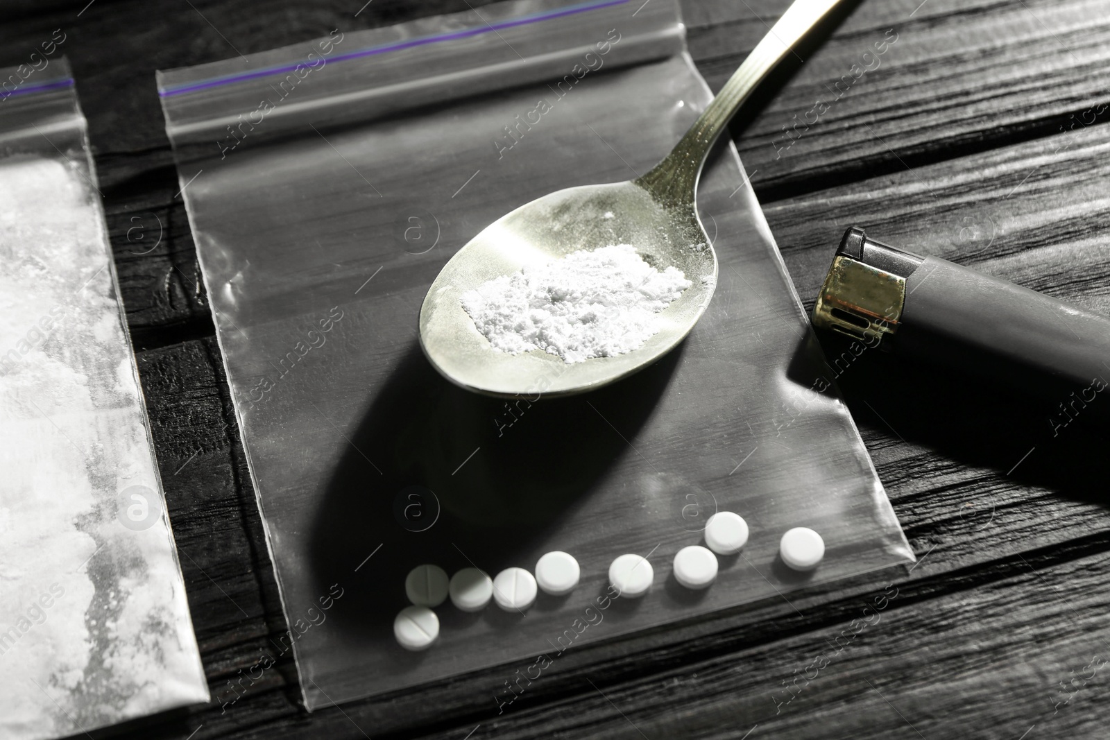 Photo of Drug addiction. Spoon bag with powder, cigarette lighter and pills on black wooden table, closeup