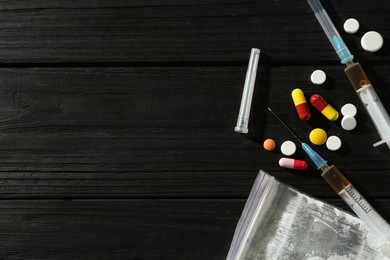 Photo of Drug addiction. Plastic bag with powder, syringes and pills on black wooden table, flat lay. Space for text