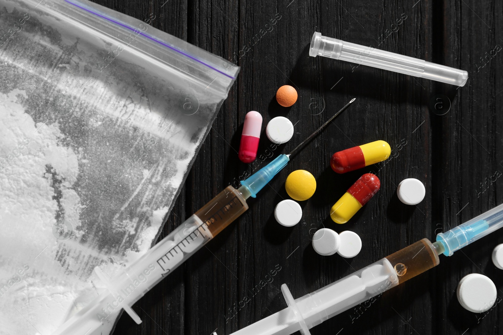 Photo of Drug addiction. Plastic bag with powder, syringes and pills on black wooden table, flat lay