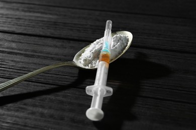 Photo of Drug addiction. Spoon with powder and syringe on black wooden table, closeup