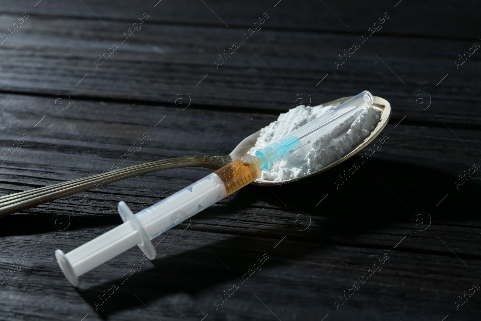 Photo of Drug addiction. Spoon with powder and syringe on black wooden table, closeup