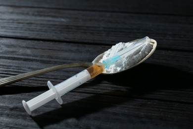 Photo of Drug addiction. Spoon with powder and syringe on black wooden table, closeup