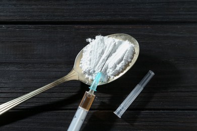 Photo of Drug addiction. Spoon with powder and syringe on black wooden table, closeup