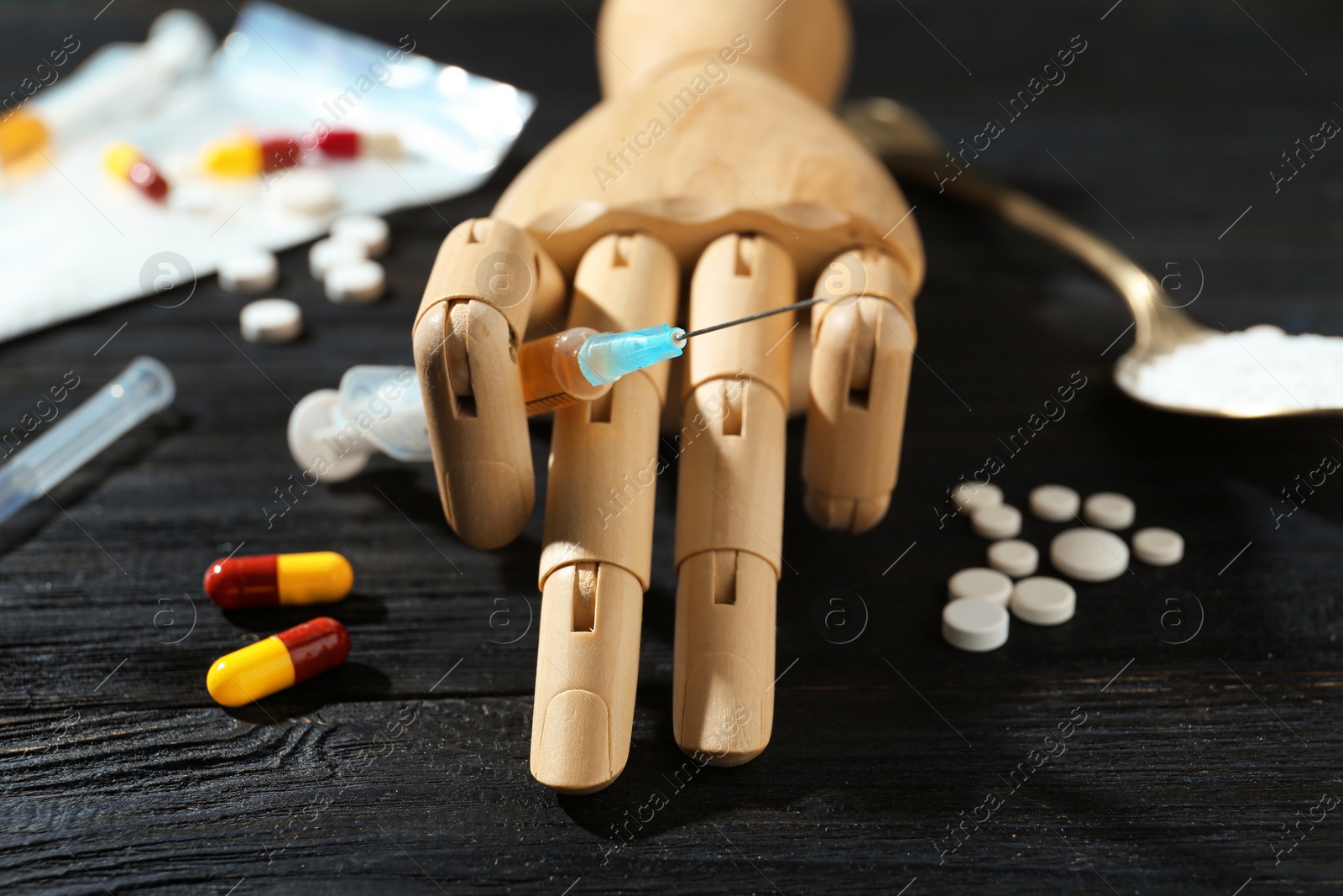 Photo of Drug addiction. Mannequin hand with syringe and pills on black wooden table, closeup