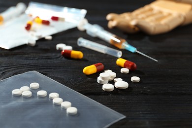 Photo of Drug addiction. Plastic bag with pills on black wooden table, closeup