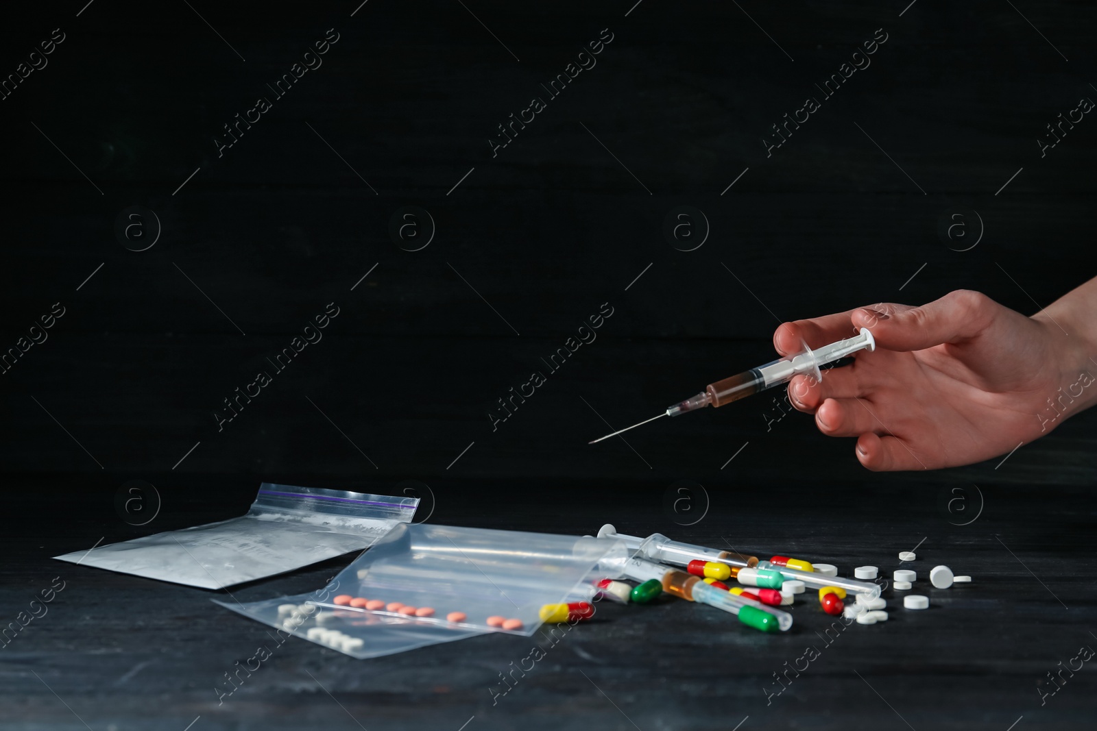 Photo of Drug addiction. Woman with syringe at black wooden table against dark background, closeup. Space for text