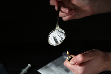 Photo of Drug addiction. Woman lighting spoon with powder against dark background, closeup. Space for text