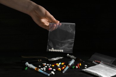 Photo of Drug addiction. Woman holding plastic bag with pills against dark background, closeup