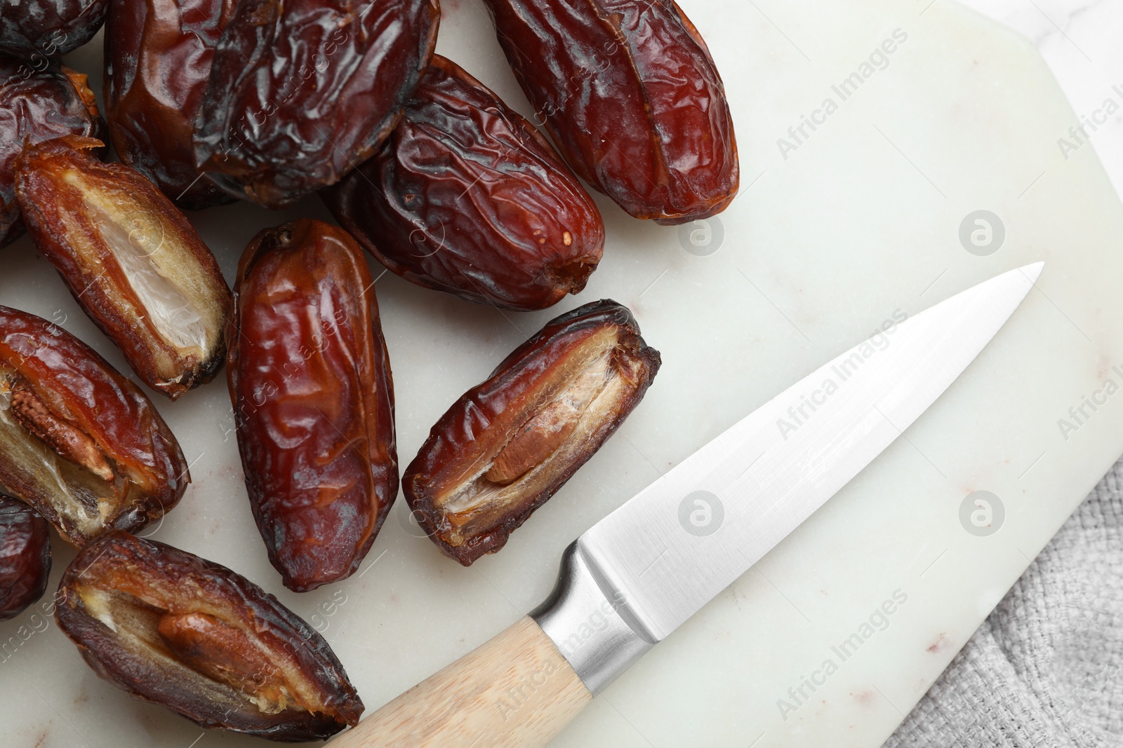 Photo of Many tasty dried dates, cutting board and knife on table, top view