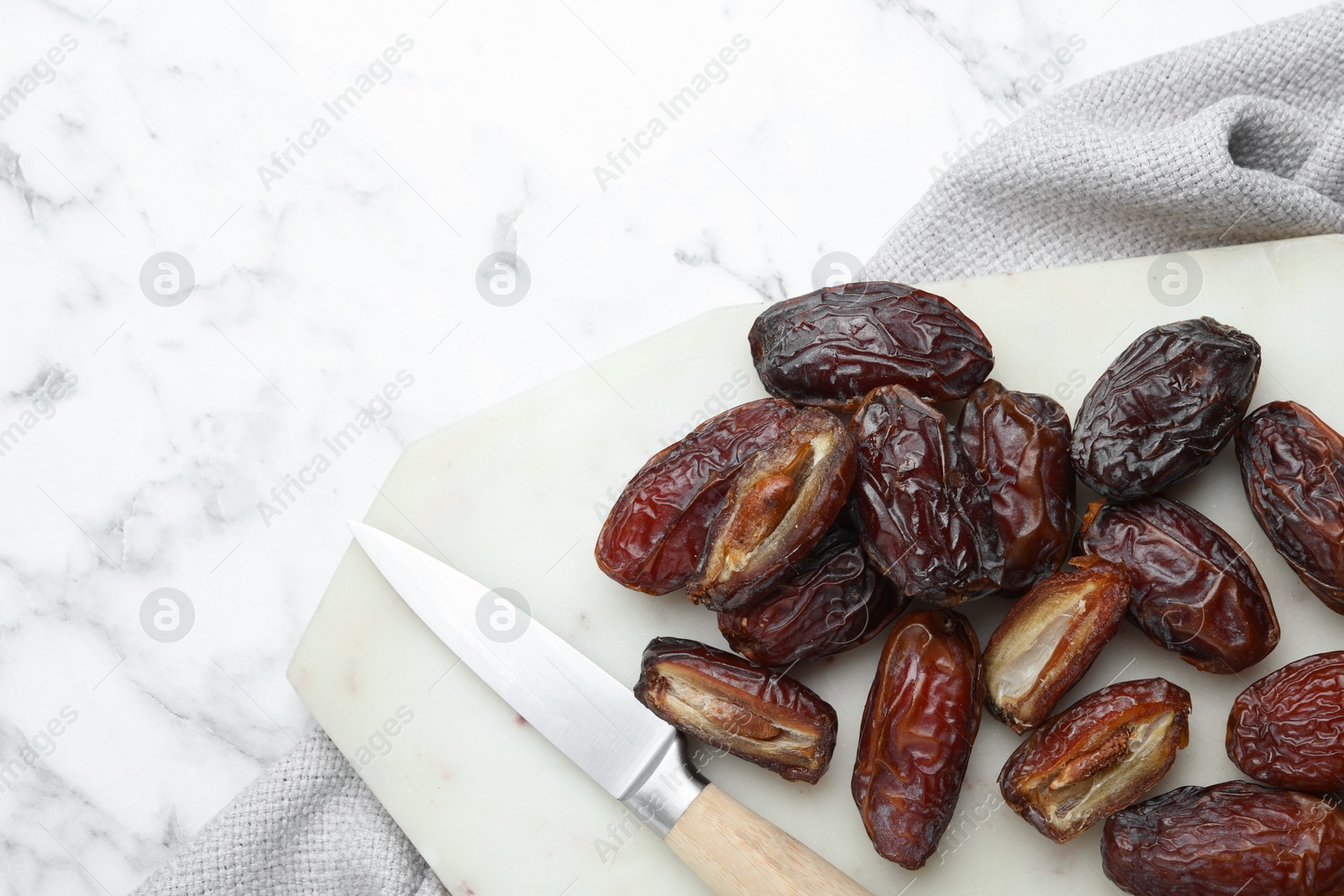 Photo of Many tasty dried dates, cutting board and knife on white marble table, top view. Space for text