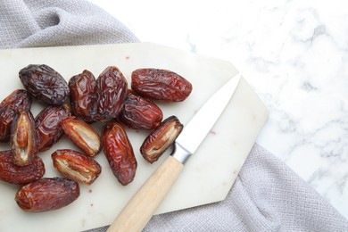 Photo of Many tasty dried dates, cutting board and knife on white marble table, top view