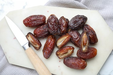 Photo of Many tasty dried dates, cutting board and knife on table, top view