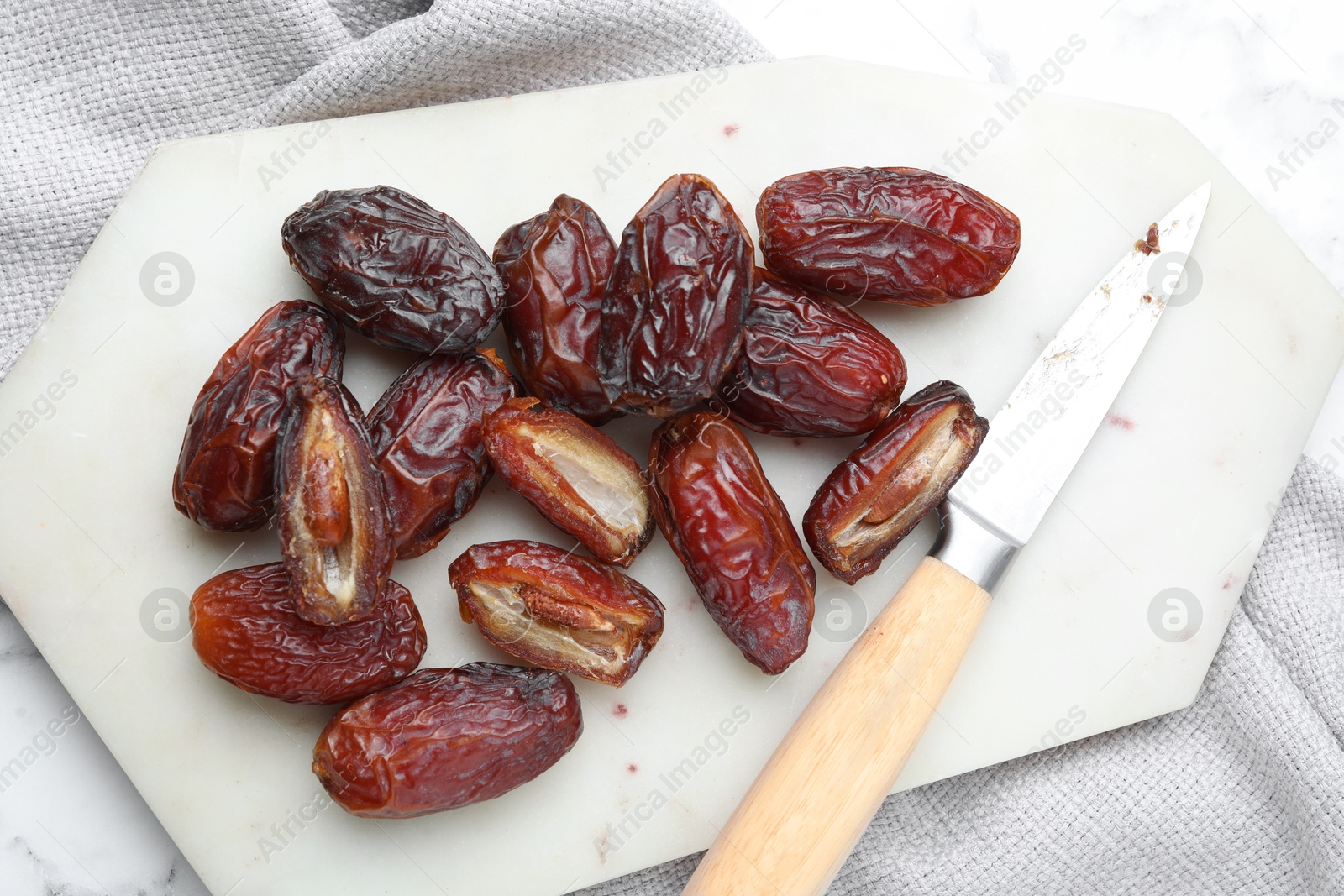 Photo of Many tasty dried dates, cutting board and knife on table, top view