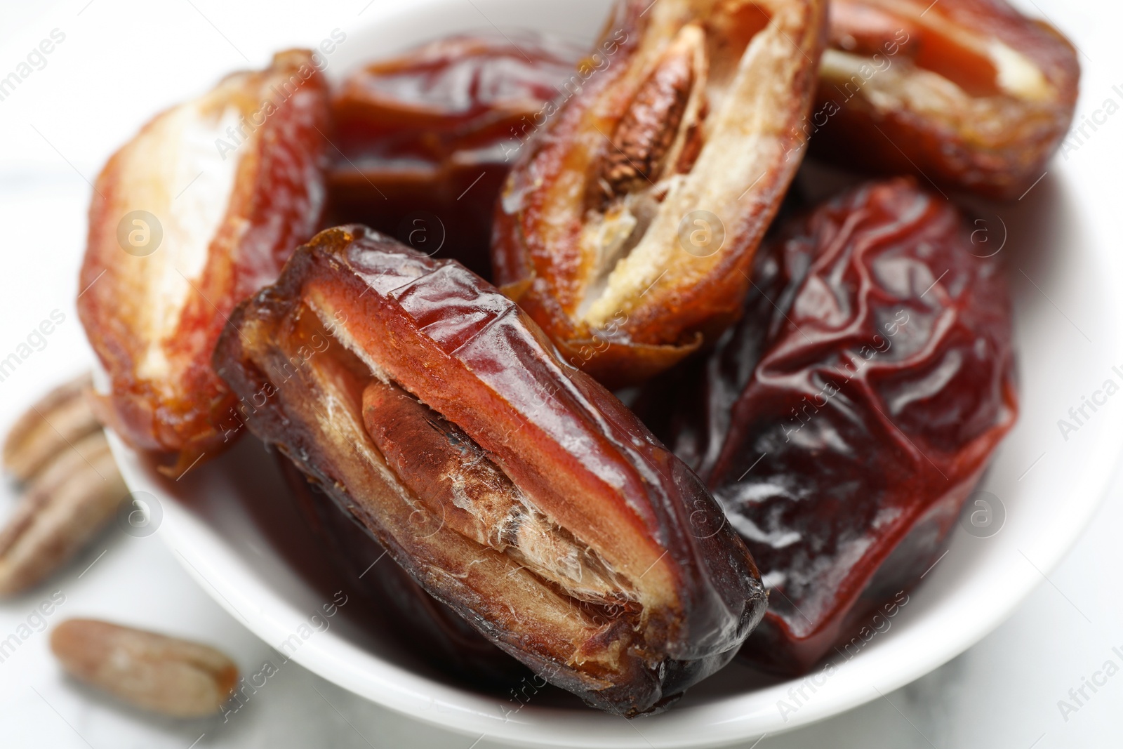 Photo of Many tasty dried dates in bowl on light table, closeup