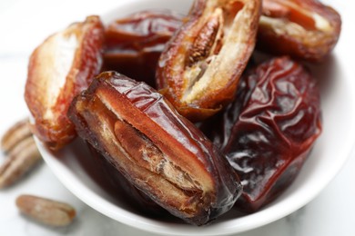 Photo of Many tasty dried dates in bowl on light table, closeup