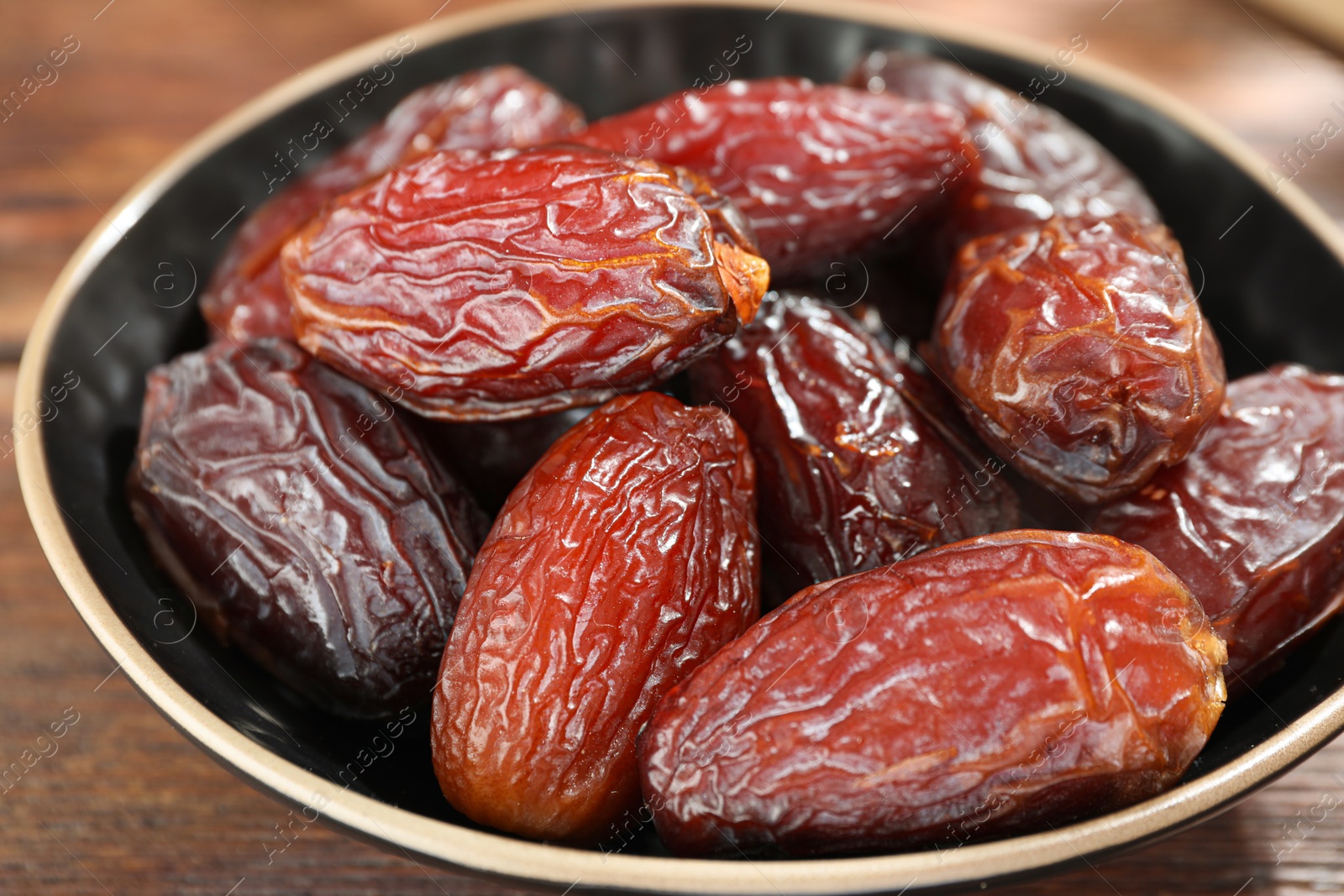 Photo of Many tasty dried dates in bowl on wooden table, closeup