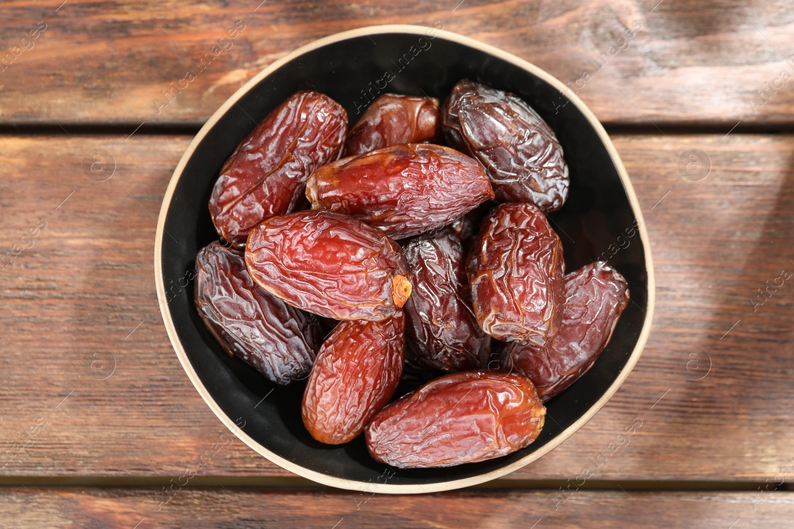 Photo of Many tasty dried dates in bowl on wooden table, top view