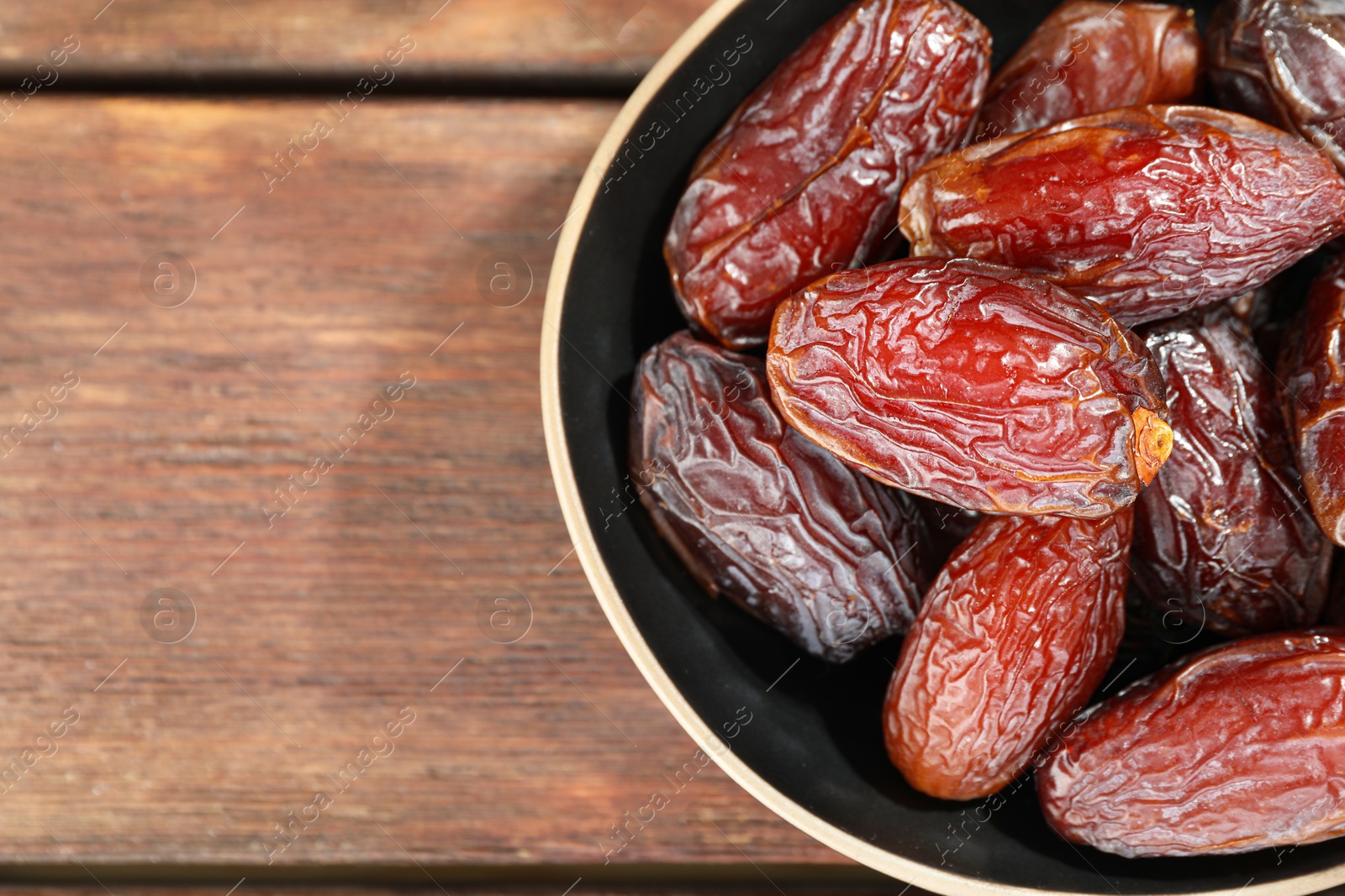 Photo of Many tasty dried dates in bowl on wooden table, top view. Space for text