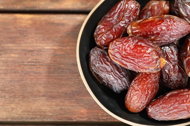 Photo of Many tasty dried dates in bowl on wooden table, top view. Space for text