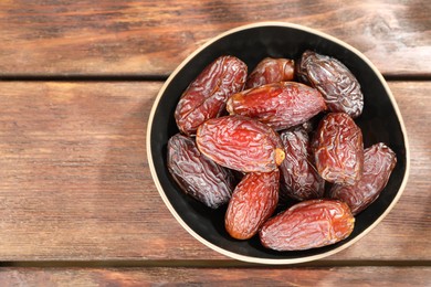 Photo of Many tasty dried dates in bowl on wooden table, top view. Space for text