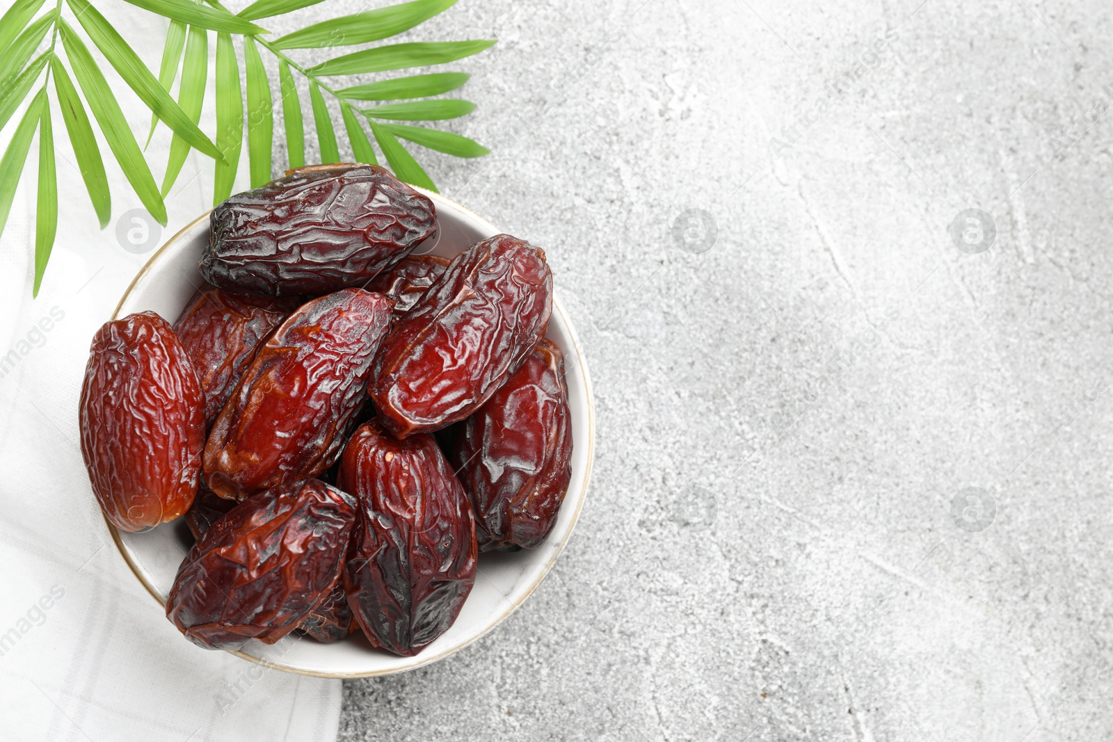 Photo of Many tasty dried dates in bowl and leaves on gray textured table, top view. Space for text