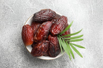 Photo of Many tasty dried dates and leaf in bowl on gray textured table, top view. Space for text