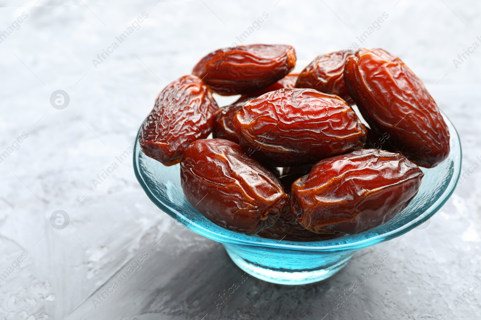 Photo of Many tasty dried dates in bowl on gray textured table, closeup