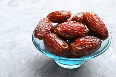 Photo of Many tasty dried dates in bowl on gray textured table, closeup