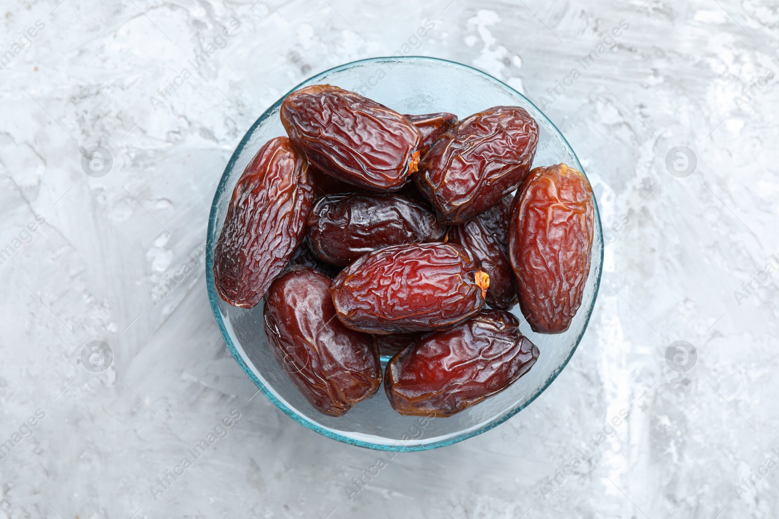 Photo of Many tasty dried dates in bowl on gray textured table, top view