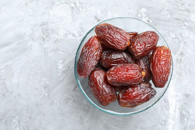 Photo of Many tasty dried dates in bowl on gray textured table, top view. Space for text