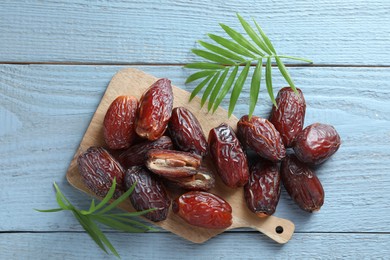 Photo of Many tasty dried dates and leaves on blue wooden table, top view