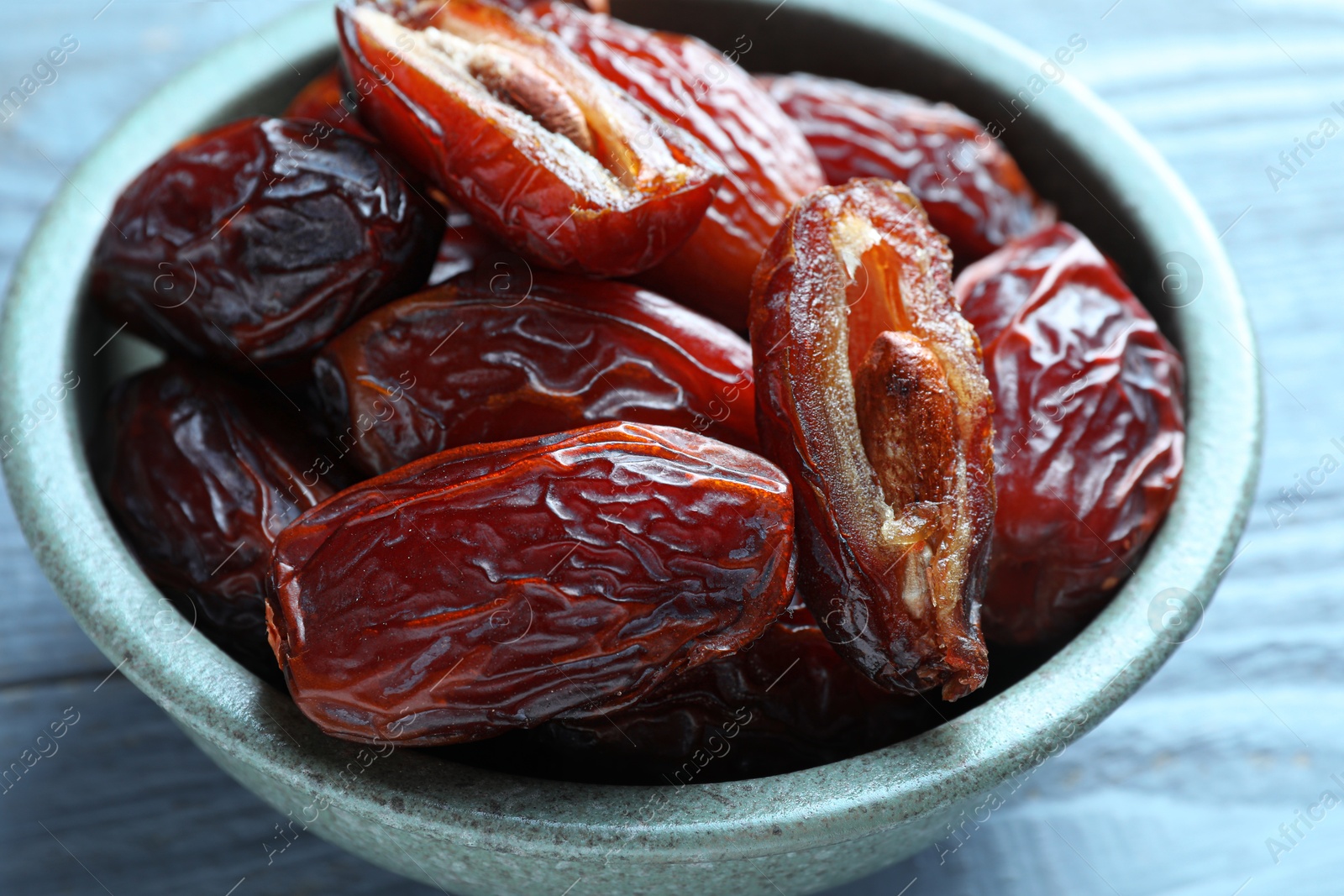 Photo of Many tasty dried dates in bowl on blue wooden table, closeup