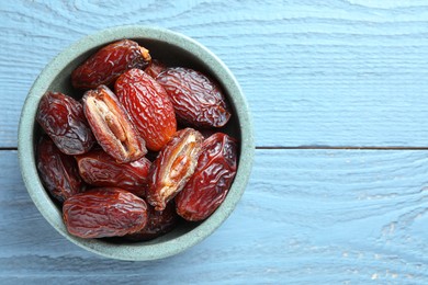 Photo of Many tasty dried dates in bowl on blue wooden table, top view. Space for text