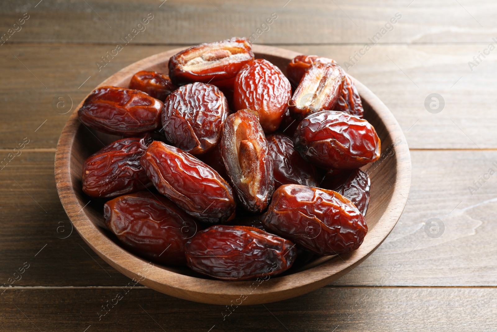 Photo of Many tasty dried dates in bowl on wooden table, closeup