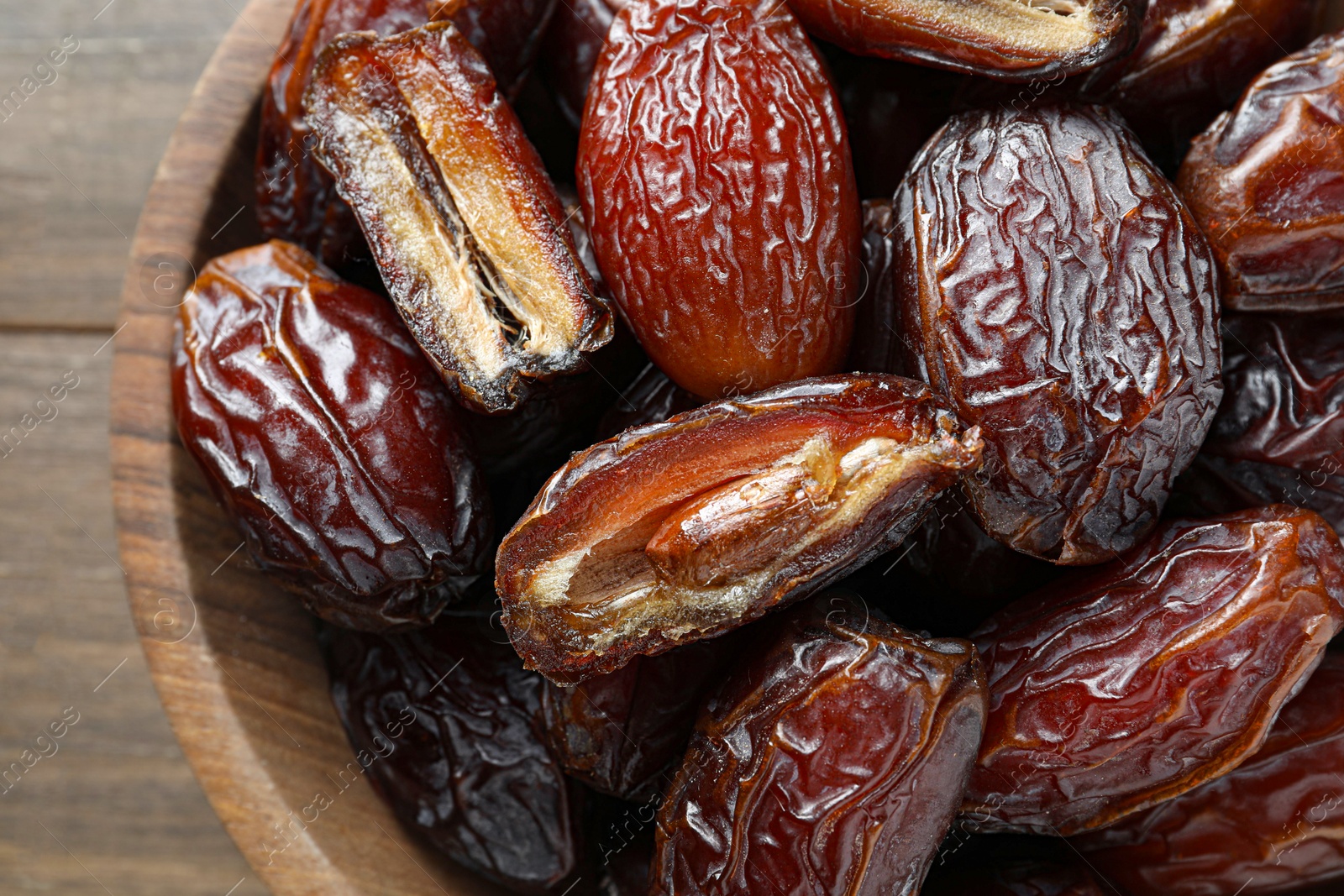 Photo of Many tasty dried dates in bowl on wooden table, top view