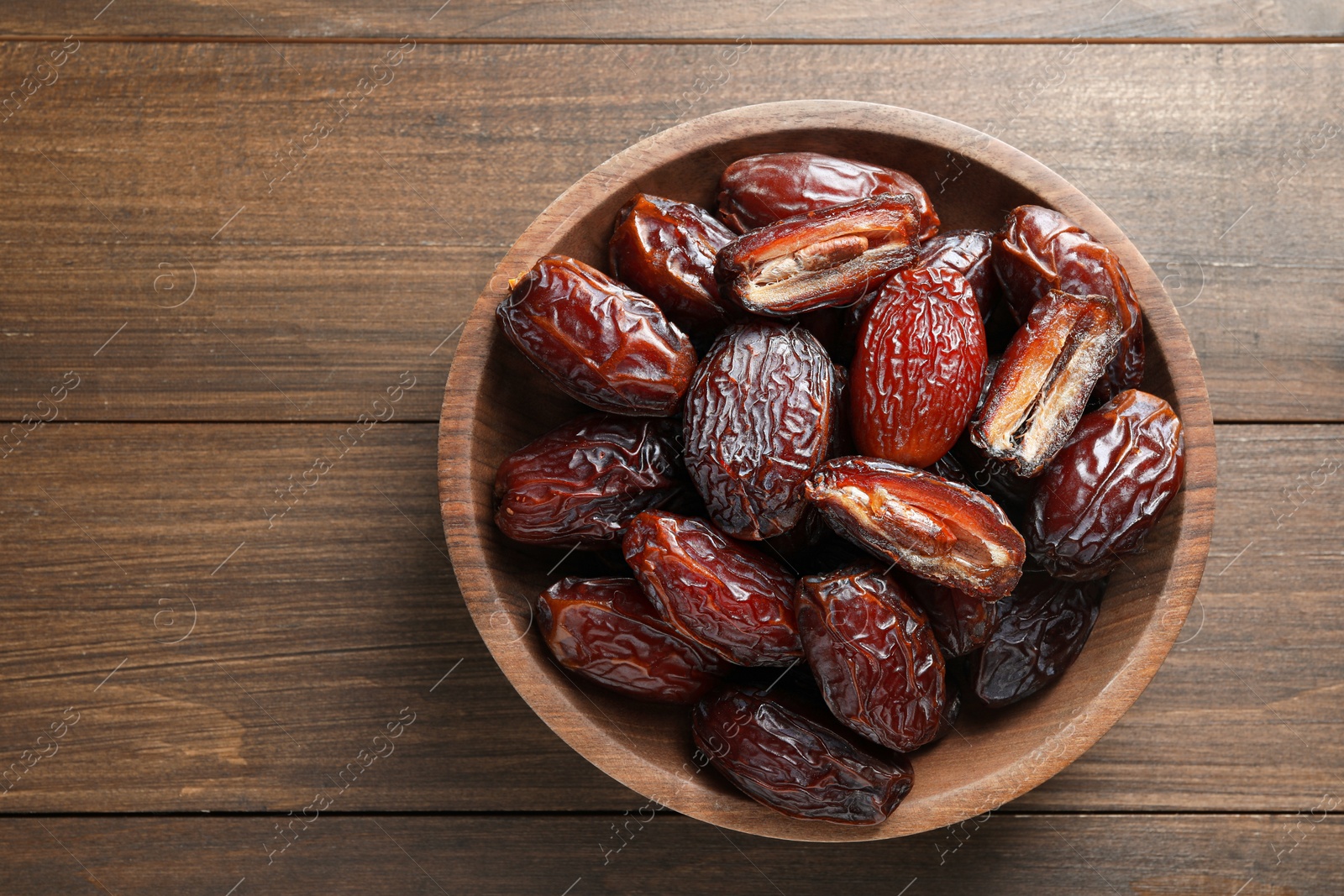 Photo of Many tasty dried dates in bowl on wooden table, top view. Space for text