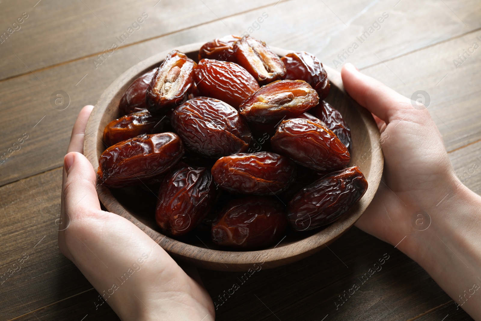 Photo of Woman with bowl of tasty dried dates at wooden table, closeup