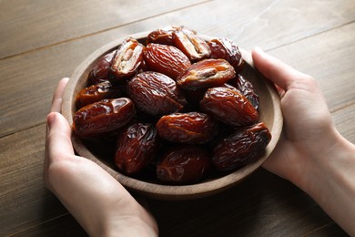 Photo of Woman with bowl of tasty dried dates at wooden table, closeup