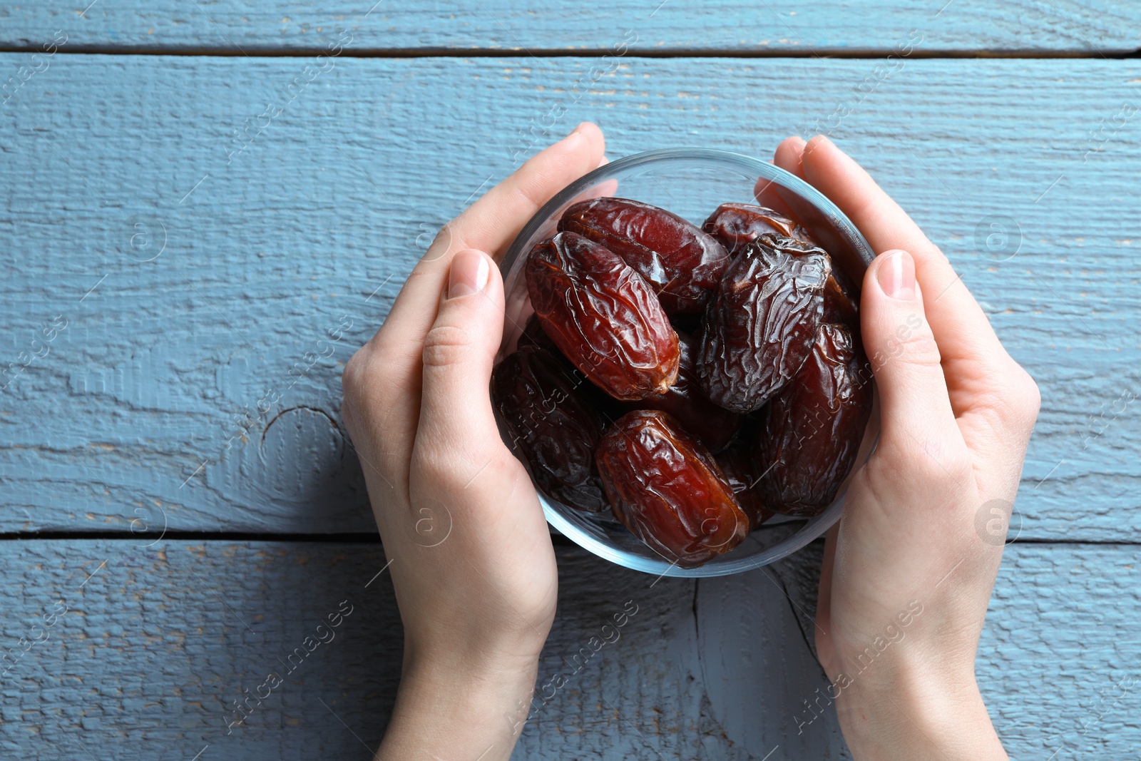 Photo of Woman with bowl of tasty dried dates at blue wooden table, top view