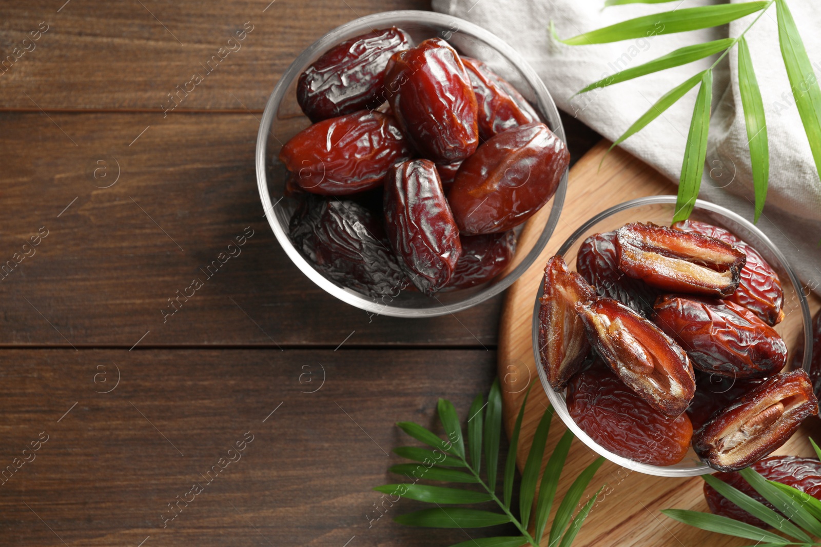 Photo of Many tasty dried dates in bowls and leaves on wooden table, flat lay. Space for text