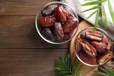 Photo of Many tasty dried dates in bowls and leaves on wooden table, flat lay. Space for text