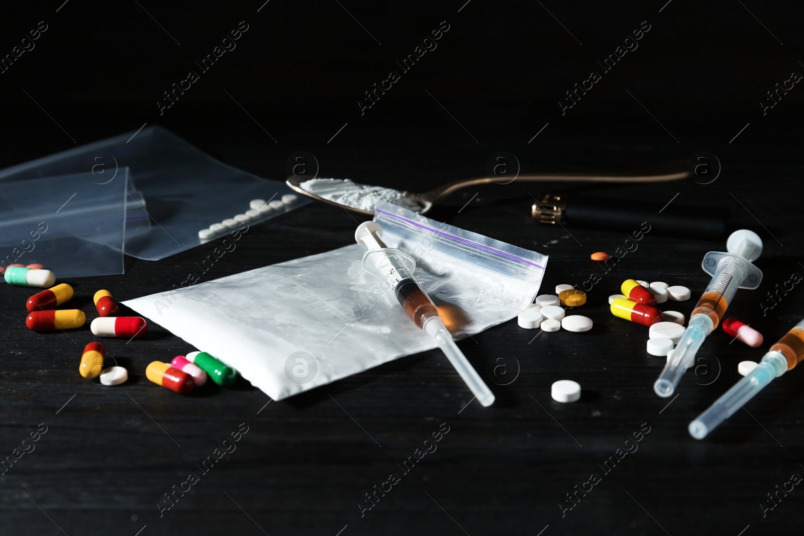 Photo of Drug addiction. Plastic bag with powder, syringes, pills and spoon on black wooden table