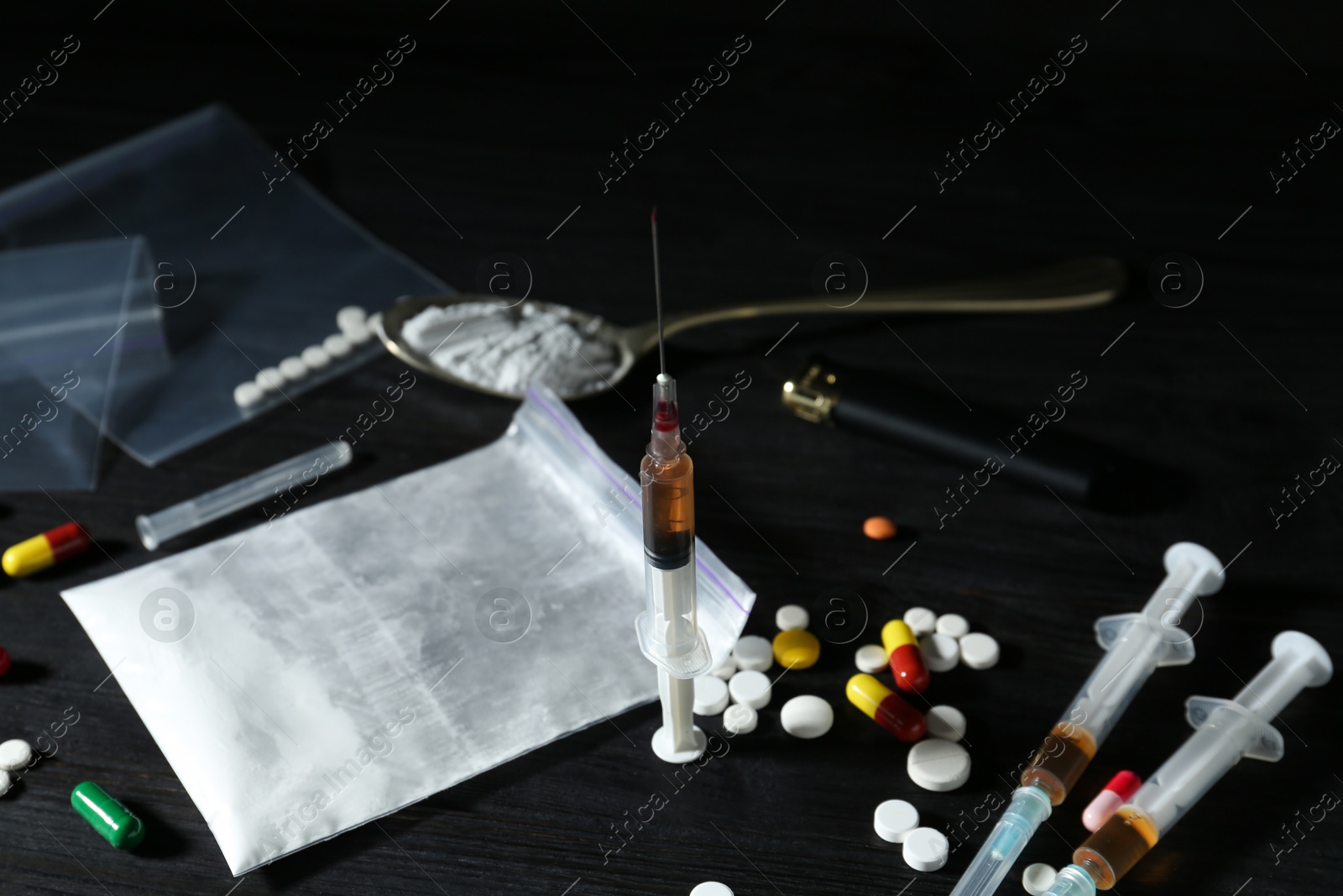 Photo of Different drugs, spoon and cigarette lighter on black wooden table, closeup