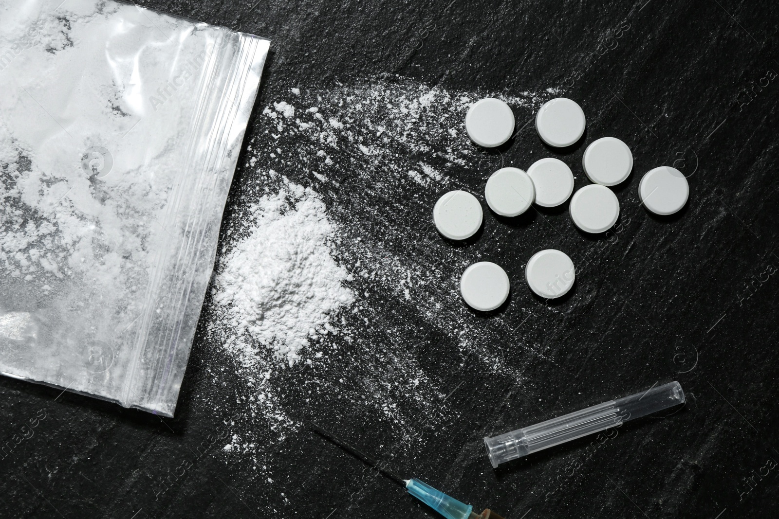 Photo of Drug addiction. Plastic bag with powder, syringe and pills on black textured table, flat lay