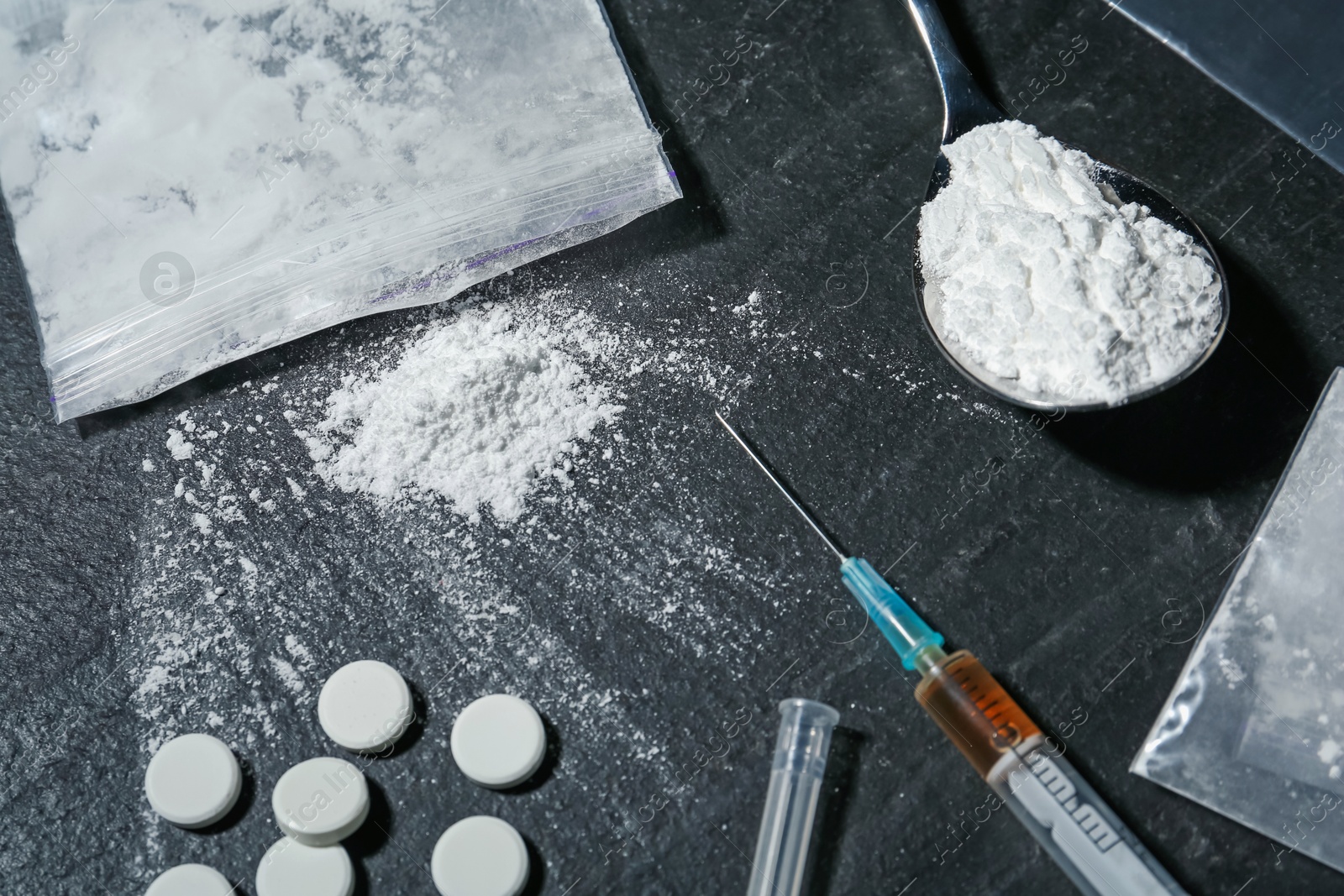 Photo of Drug addiction. Plastic bags with powder, spoon, syringe and pills on black textured table, closeup