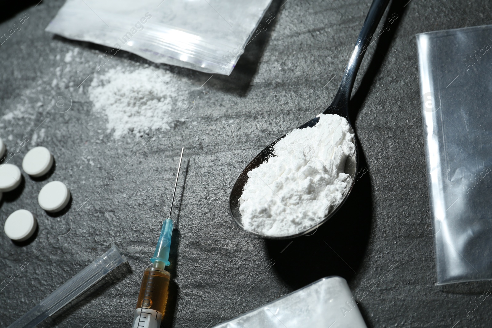 Photo of Drug addiction. Plastic bags with powder, spoon, syringe and pills on black textured table, closeup