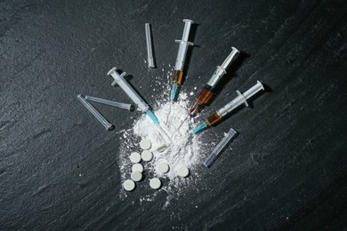 Photo of Drug addiction. Powder, pills and syringes on black textured table, flat lay