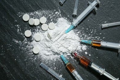 Photo of Drug addiction. Powder, pills and syringes on black textured table, flat lay